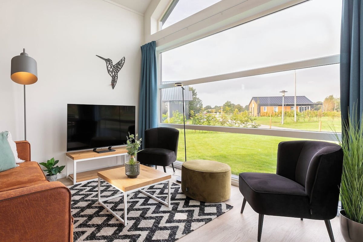 Een moderne woonkamer met een grote televisie, comfortabele zitplaatsen, een kamerbreed tapijt en uitzicht op het groen.