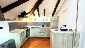 Eine kompakte Küche mit Einbauofen, Spüle und Herd. Das Zimmer verfügt über eine Holzbalkendecke und ein kleines Fenster.