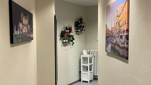 A hallway with two framed pictures on the walls, a white radiator, and a white shelf unit. - Ele rooms San Pietro (Rome)