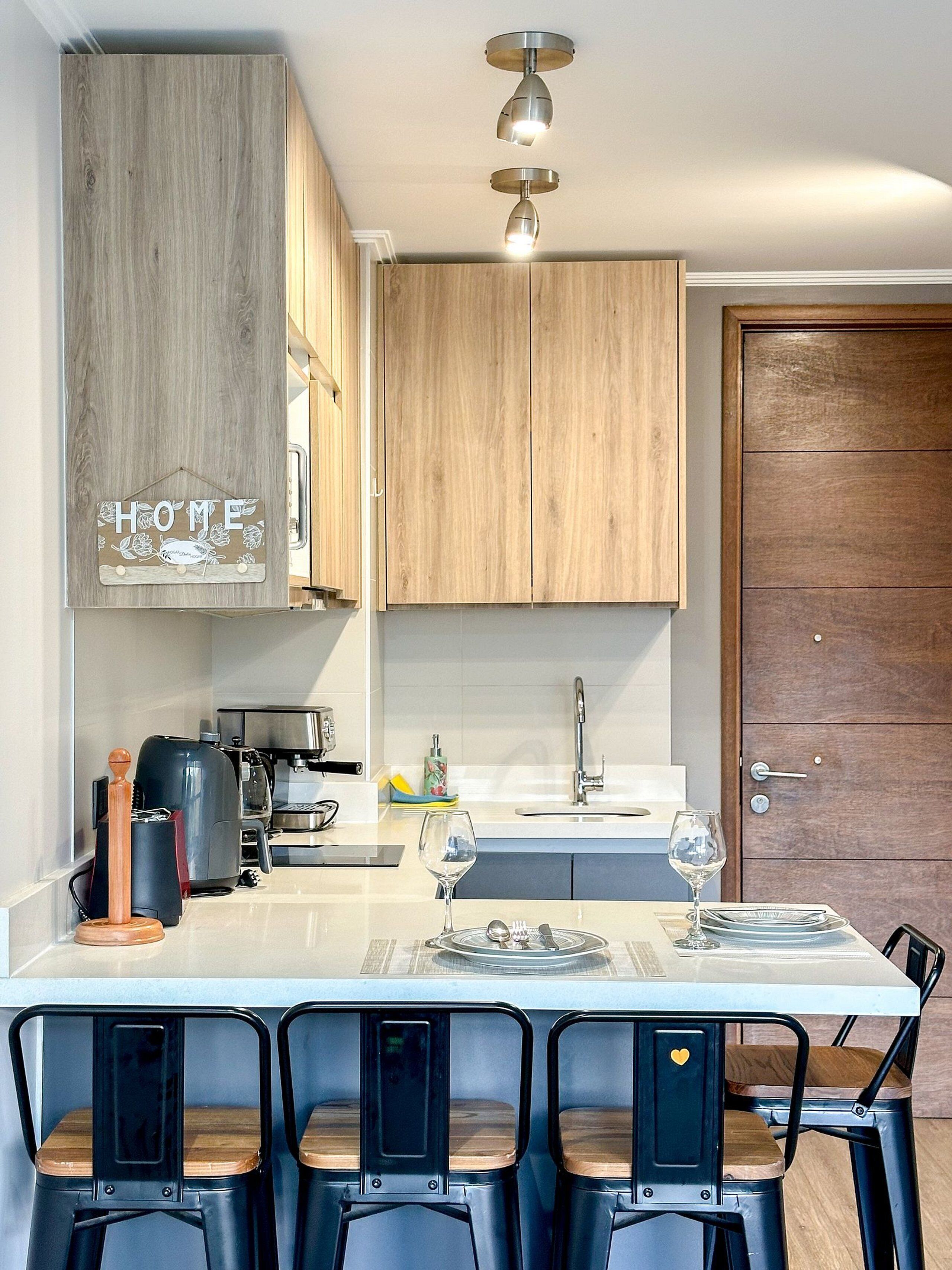 A modern kitchen with wooden cabinets, a coffee machine, a sink, and a dining area with bar stools.