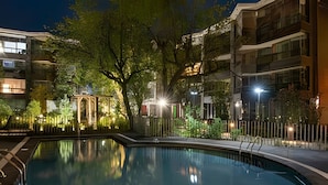 Una piscina iluminada por la noche, rodeada de árboles y edificios.