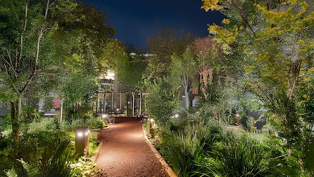 Un sendero de jardín iluminado por la noche, con un banco de madera y un pabellón.
