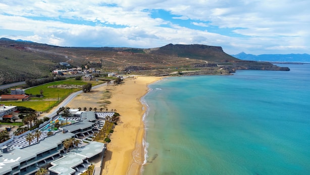 Une station balnéaire dotée d’une plage, de bâtiments modernes et bordée par une chaîne de montagnes.