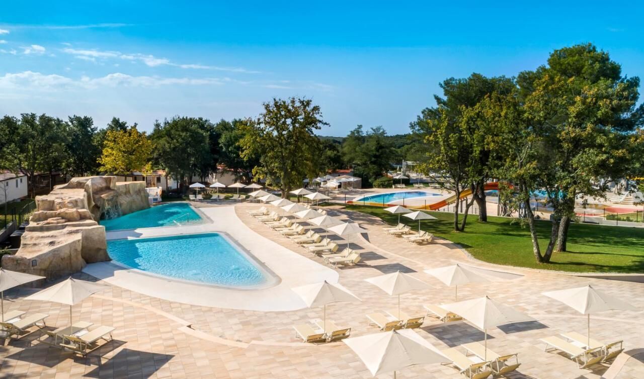 Un complex turístic amb diverses piscines, gandules i ombrelles.