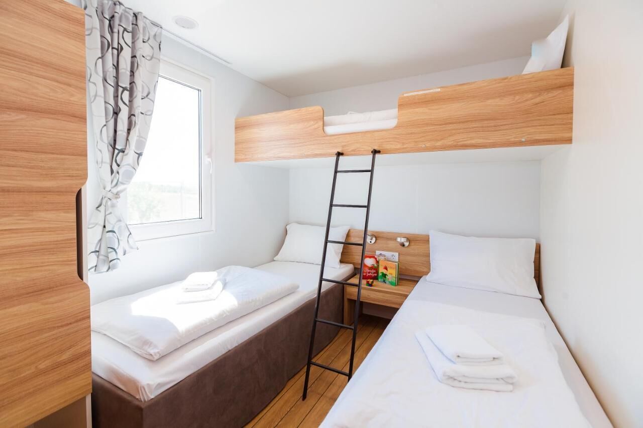 A compact room with bunk beds, a ladder, a small table with a box, and a window with curtains.