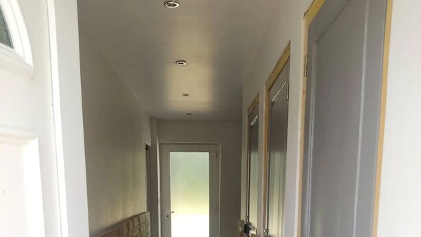 A hallway with a tiled floor, wooden paneling on the walls, and doors with wooden handles.