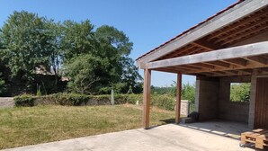 A covered patio area with a concrete floor, wooden beams, and a view of a grassy yard with trees.