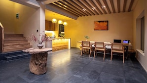 Un interior moderno con un mostrador de recepción de madera, una zona de comedor con sillas, un cuadro grande en la pared y una escalera que sube a otro nivel.
