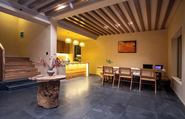A modern interior with a wooden reception desk, a dining area with chairs, a large painting on the wall, and a staircase leading to another level. - Shanghai Xingshe Camping Guesthouse (Shanghai)