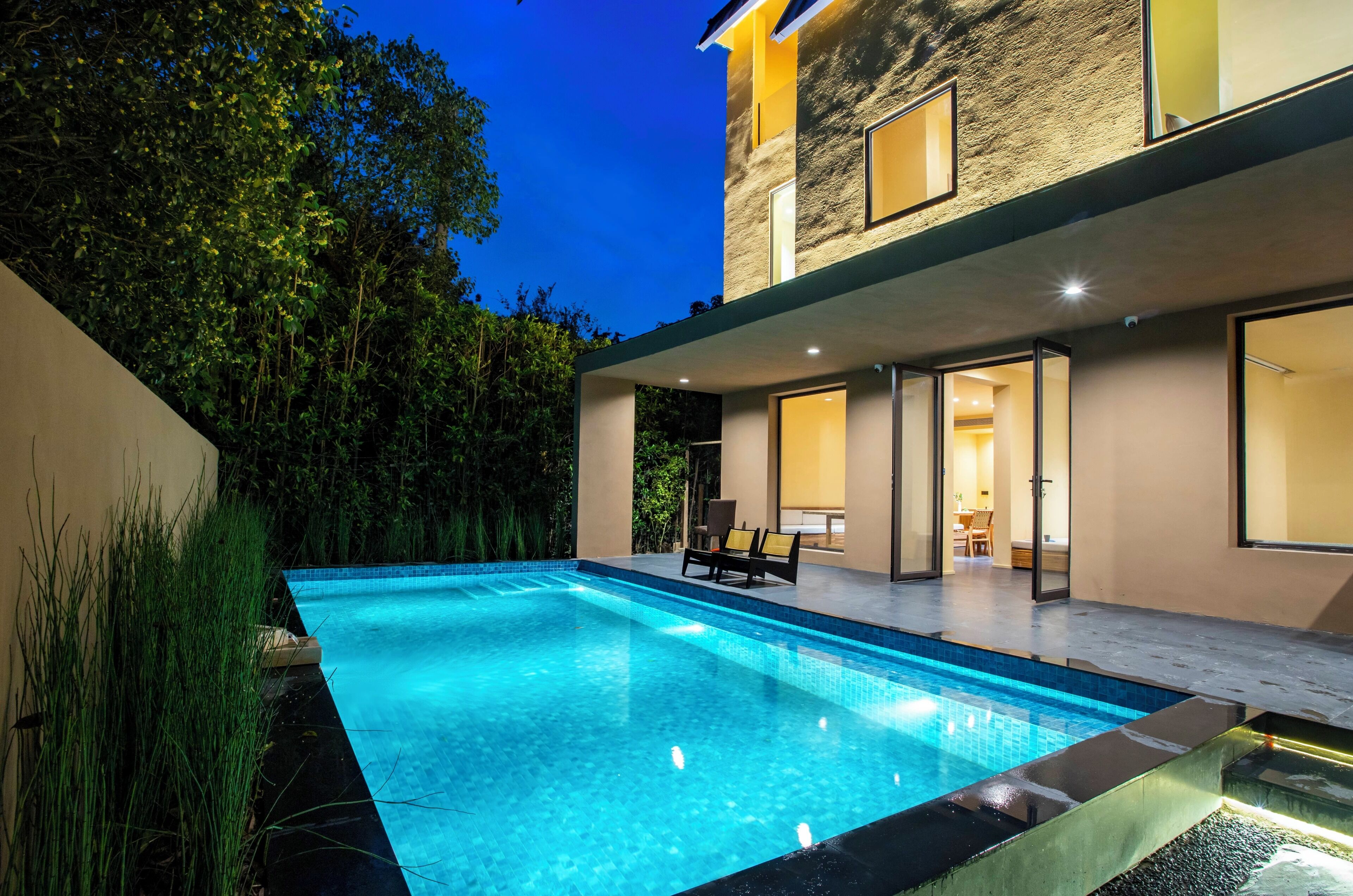 Uma casa moderna com piscina, um alpendre com cadeiras e interior bem iluminado.