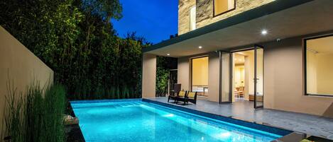 Uma casa moderna com piscina, um alpendre com cadeiras e interior bem iluminado.