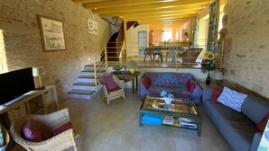 A spacious living area with a staircase leading to an upper level, wicker furniture, and a television on a stand. - Beautiful house with heated pool. Quiet location, close to attractions. (Bouzic)