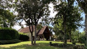 A rustic wooden house with a sloped roof, surrounded by a well-maintained lawn and mature trees. - Beautiful house with heated pool. Quiet location, close to attractions. (Bouzic)