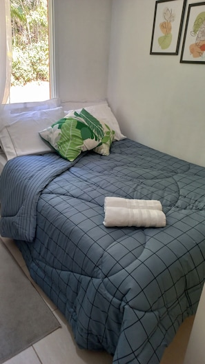 Een net opgemaakt bed met een blauwe quilt, een kussen met bladmotief en een witte gevouwen handdoek.