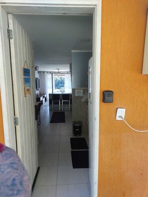Een gang die leidt naar een keuken, met een koelkast, een prullenbak en een stopcontact op de muur.