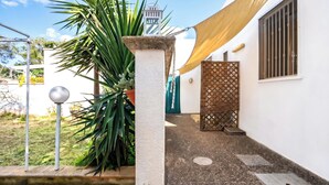 A courtyard with a white wall, a metal gate, a palm tree, and a yellow shade cloth.