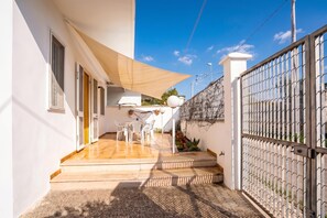 Un patio techado al aire libre con una mesa, sillas, una escalera y un acceso con portón.