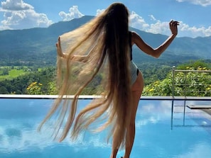 Une personne se tient près d’une piscine, avec un paysage montagneux en arrière-plan.