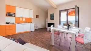 Een moderne keuken met witte en oranje kastjes, een magnetron en een eethoek met een tafel en stoelen.