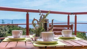 A table set with white cups and saucers, a silver teapot, and a potted plant on a wooden deck with a view of the sea and mountains. - LIME - E&T apartments with a beautiful pool (Rabac)