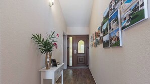 A hallway with a wooden floor, a white console table with a vase of flowers, and a door with a glass panel. - LIME - E&T apartments with a beautiful pool (Rabac)