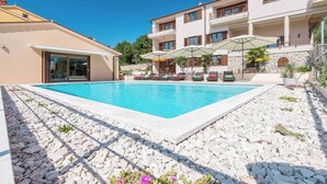 A swimming pool with lounge chairs and umbrellas, surrounded by a stone-tiled deck and a building with balconies. - RED - E&T apartments with a beautiful pool (Rabac)