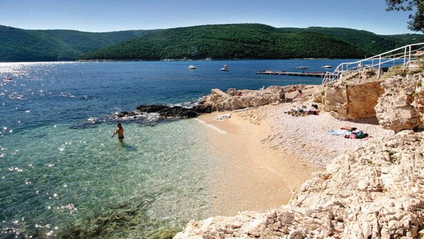 A beach with clear water, rocky shore, and boats in the distance. - RED - E&T apartments with a beautiful pool (Rabac)