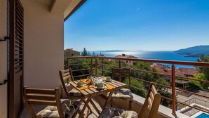 A balcony with a table set for two, overlooking a scenic view of the sea and hills.