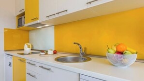 A kitchen with a sink, a fruit bowl, and a kettle on the counter.
