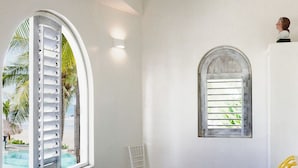 A room with a bed, a ceiling fan, a window with shutters, and a view of palm trees. - Casablanca Beachfront Gateway (Troncones)