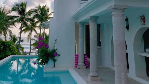 A pool area with a clear view of the ocean, surrounded by palm trees and a white building with columns. - Casablanca Beachfront Gateway (Troncones)
