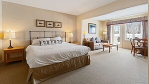 A hotel room with a large bed, a sofa, a dining table, and a chair. There are framed pictures on the wall and a window with curtains. - Peaceful Escape King Bed and Outdoor Activities (Shanty Bay)