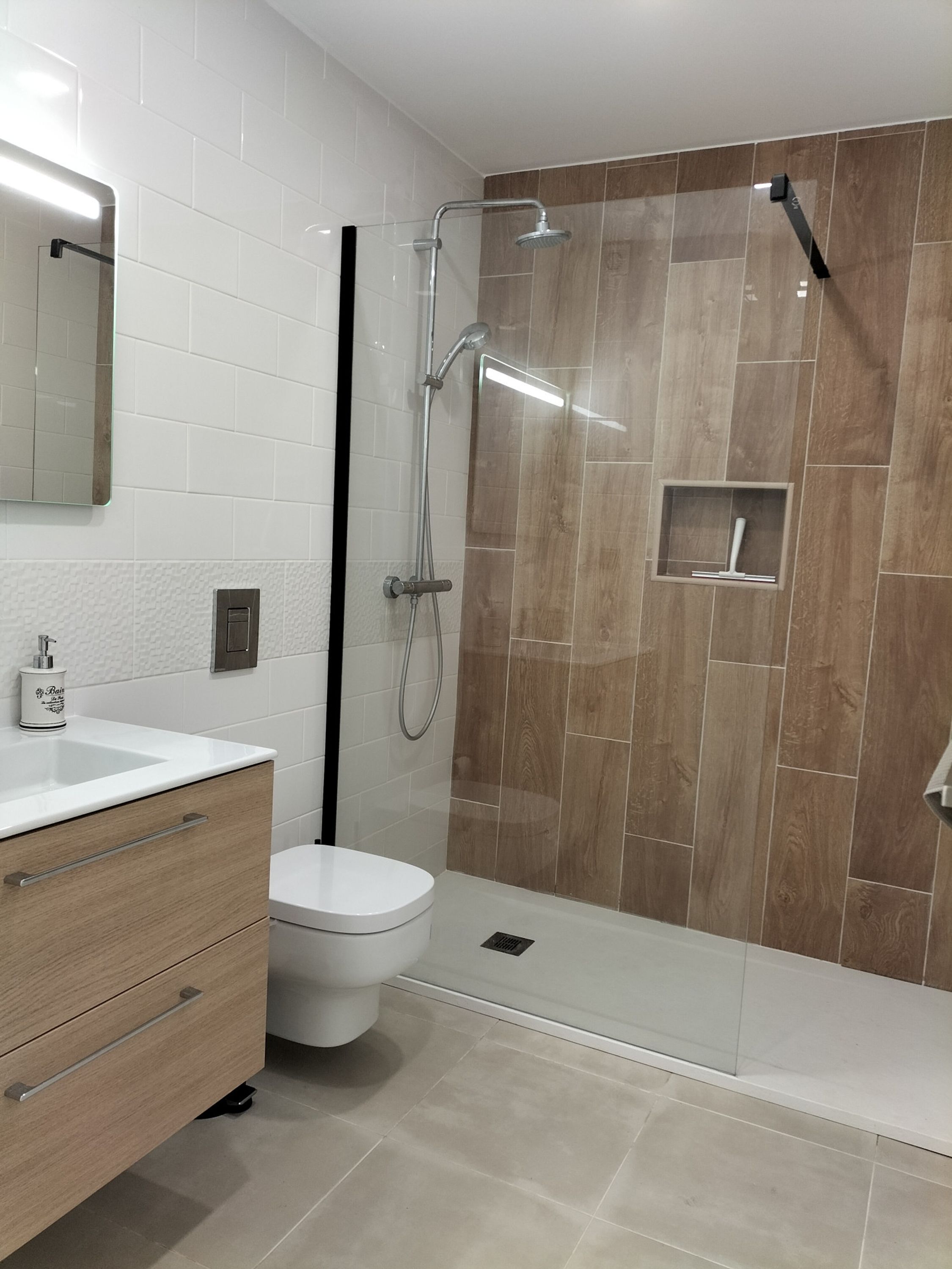 Un baño moderno con cabina de ducha de vidrio, inodoro blanco y tocador de madera con espejo.