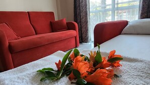 Una camera d'albergo con un divano rosso, un tappeto soffice bianco e una finestra con tende leggere.