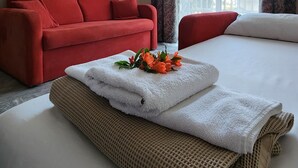 Una camera d'albergo con un letto, un divano rosso, un quadro appeso al muro e una finestra con tende.