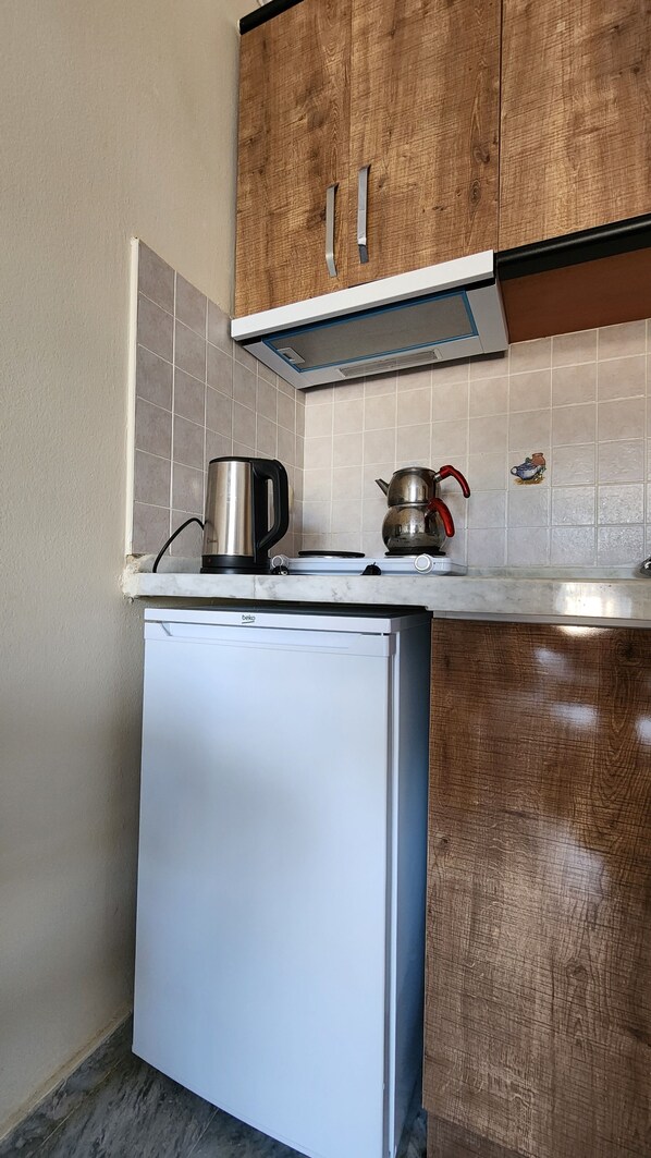 A compact kitchen with a white refrigerator, a kettle, and a pot on the countertop.