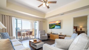 A spacious living room with a large sofa, a coffee table, and a dining area with chairs. There is a painting on the wall and a ceiling fan. - Stunning 3 Bed Apartment - Reunion Resort (Kissimmee)