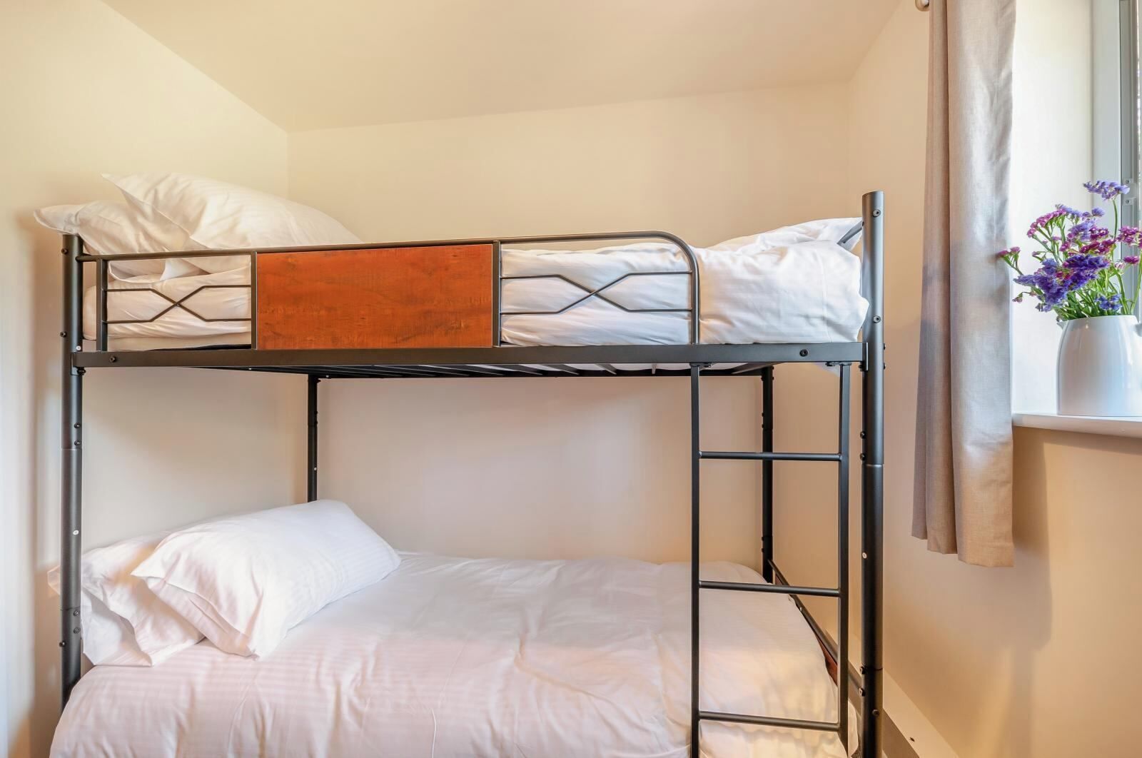 Quarto com beliche, janela e um vaso de flores.