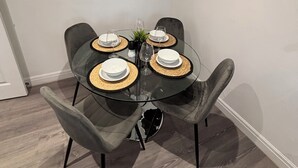 A dining area with a round glass table, four grey upholstered chairs, and a round mirror on the wall.