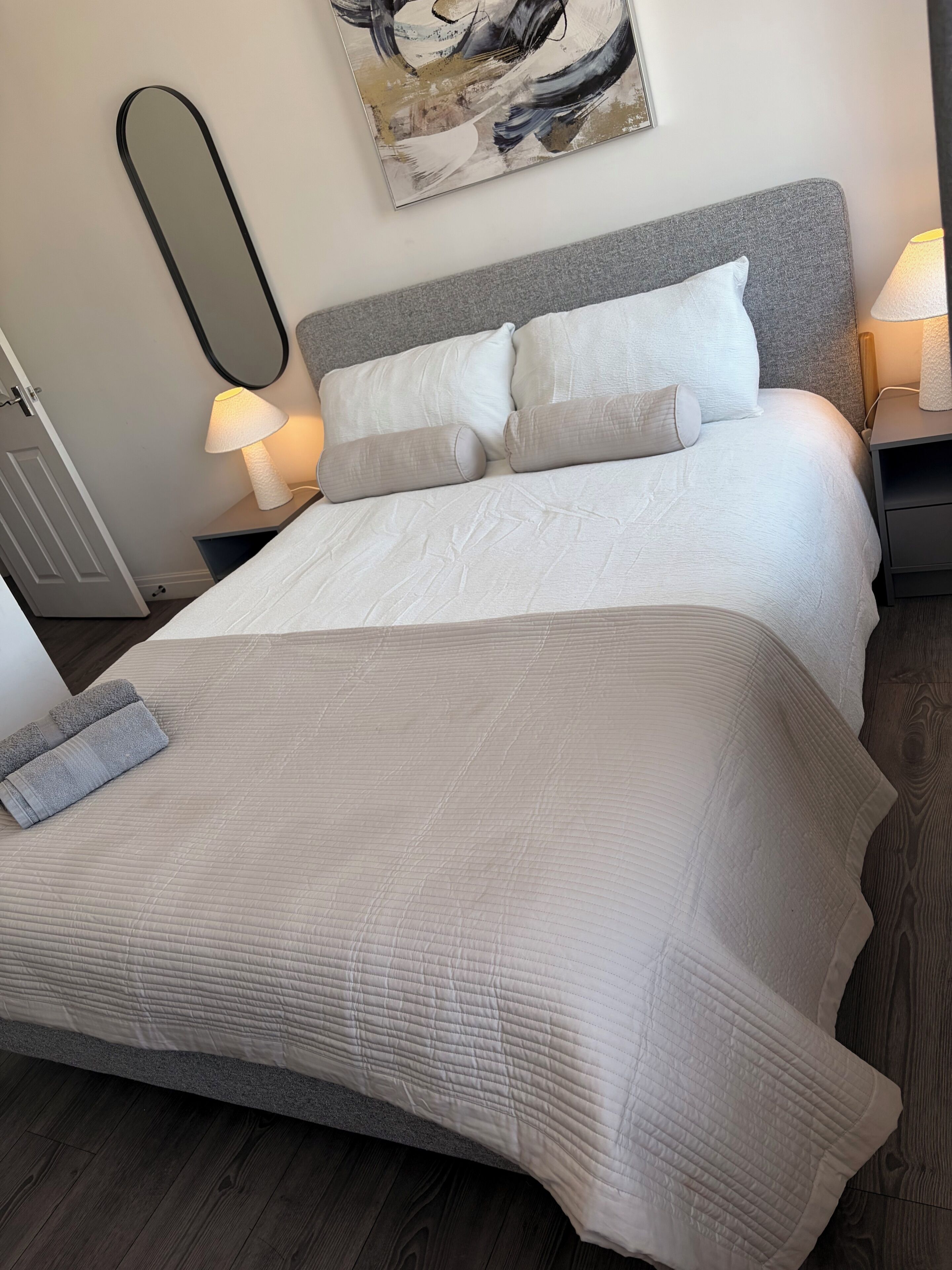 A bed with a quilted cover, two bedside lamps, and a painting on the wall.