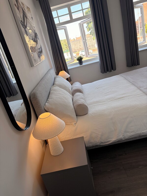 A bedroom with a bed, a bedside lamp, a mirror, and a window with curtains.