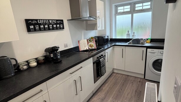 A modern kitchen with white cabinets, a black countertop, a coffee menu sign, and a window with a view.