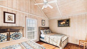 Een slaapkamer met een houten plafond, een bed met beddengoed met een patroon, een stoel en twee ingelijste foto's aan de muur.
