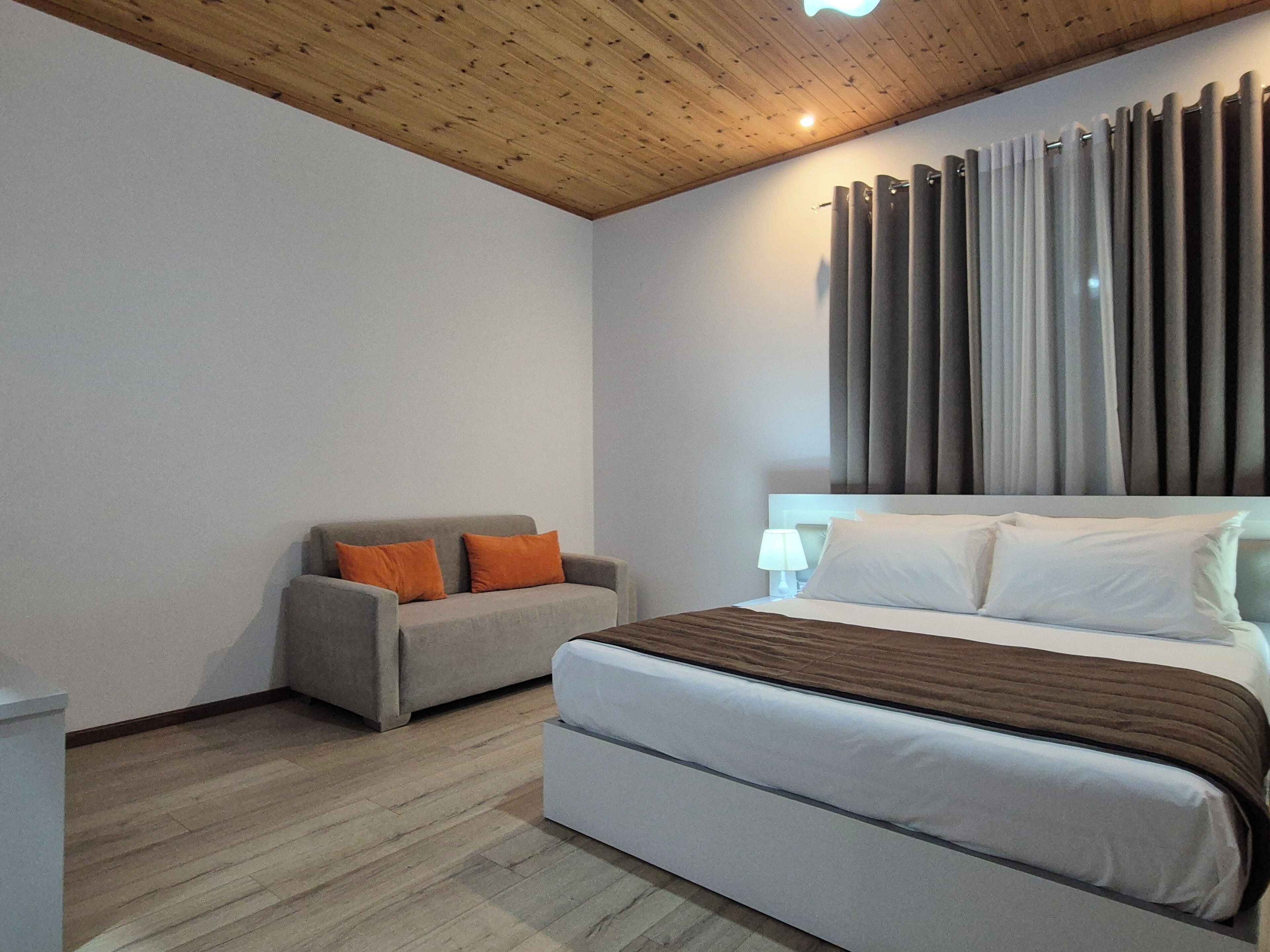 Un dormitorio con cama, sofá, suelo de madera y techo de madera.