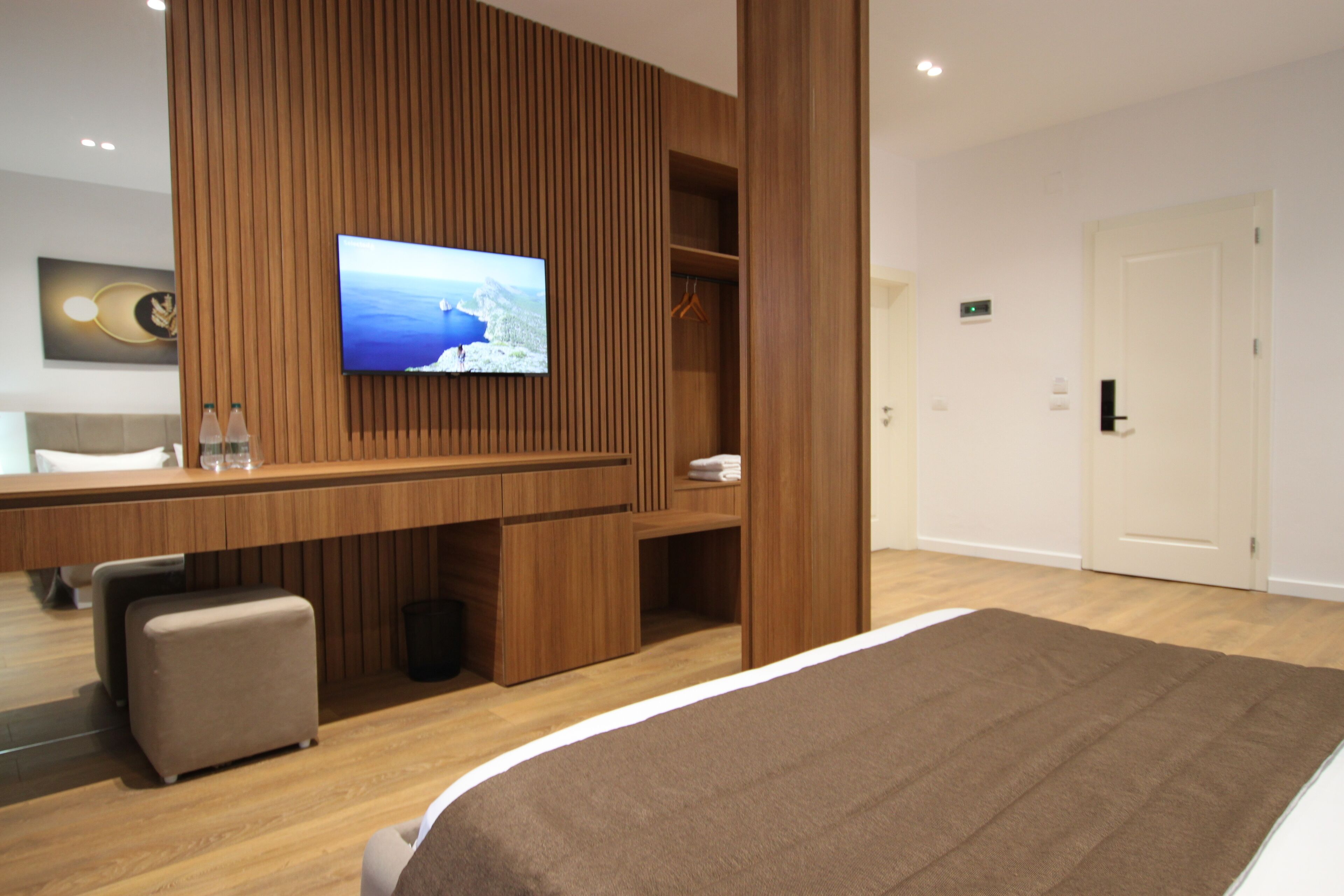 A modern hotel room with a large bed, a wooden panel wall, a flat-screen TV, a desk with a chair, and a small seating area.