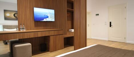 A modern hotel room with a large bed, a wooden panel wall, a flat-screen TV, a desk with a chair, and a small seating area.