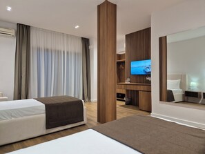 Egy modern szállodaszoba, amelyben található egy ágy, egy íróasztal televízióval, valamint egy nagy tükör.