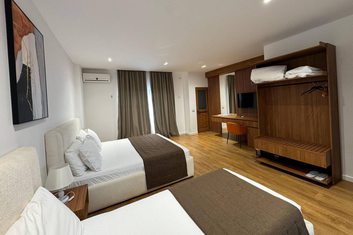 Una habitación de hotel moderna con dos camas, un escritorio, un armario y un televisor.