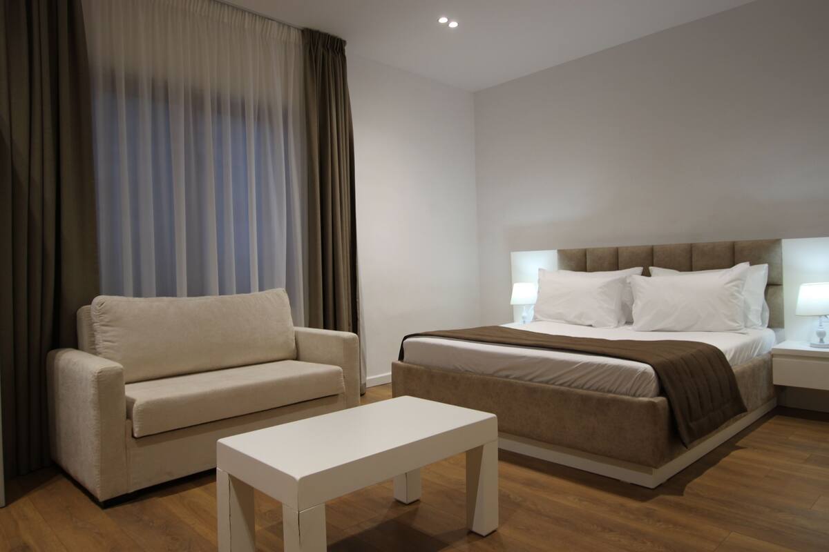 Una habitación de hotel moderna con una cama, un sofá, una mesita pequeña y una mesita de noche.