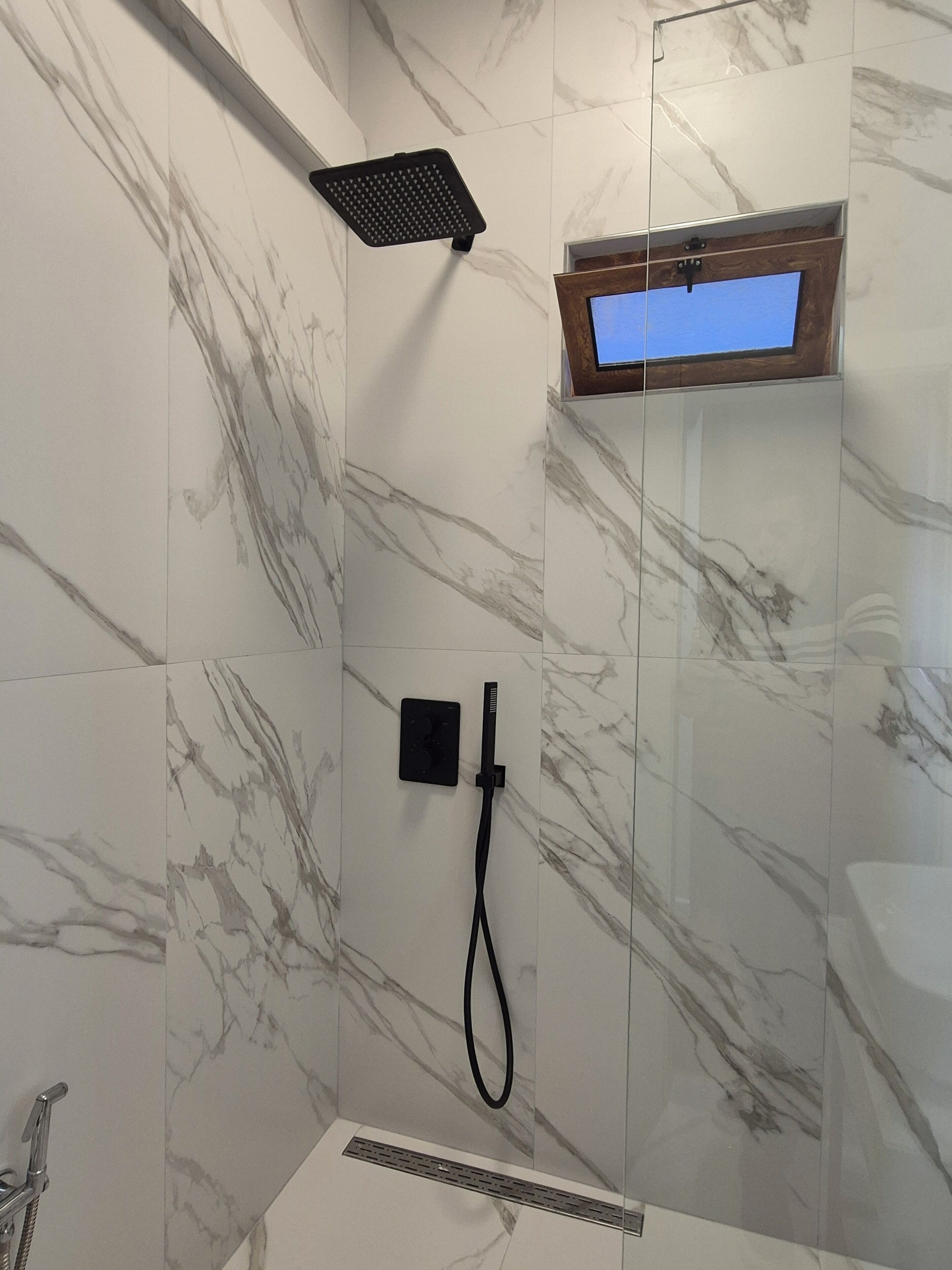 Une douche moderne dotée d’un pommeau de douche à main, d’une douchette à pluie intégrée et d’une petite fenêtre.